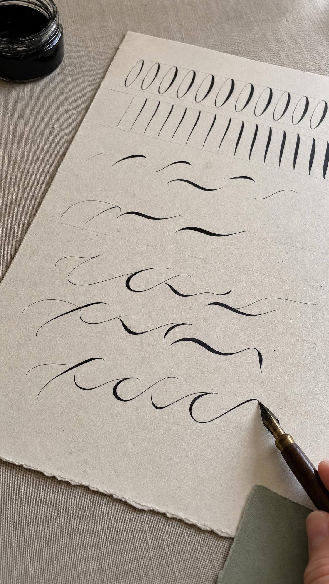 A large practice sheet covered in connected looping strokes, held steady by one hand while the other draws a continuous line with a pointed pen.